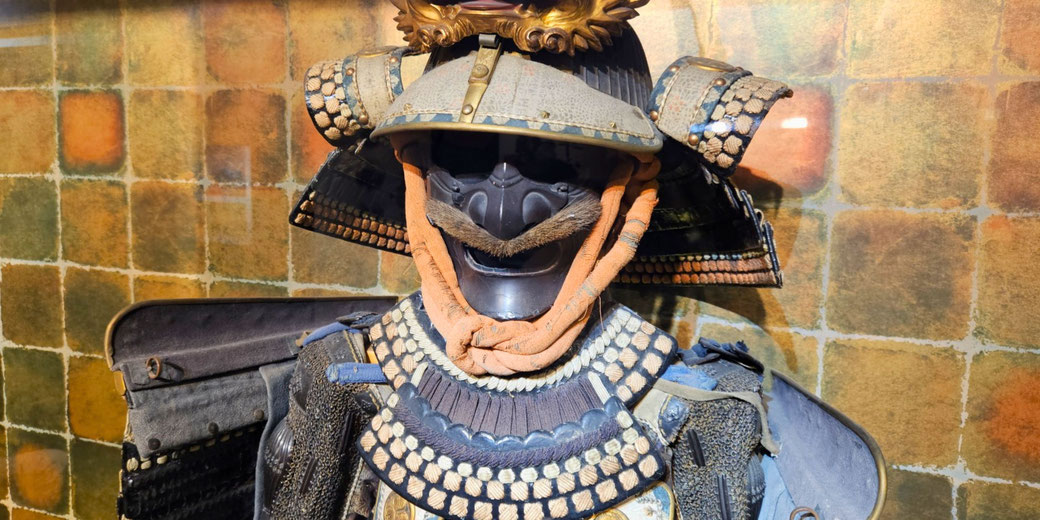 A traditional Japanese samurai armor set featuring a menacing faceplate with a mustache, a decorated helmet, and intricate woven details.