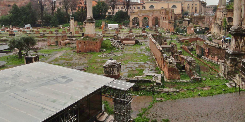 The ruins of the Roman Forum, with broken columns, brick walls, and ancient pathways. The covered Lapis Niger is visible in the bottom left.