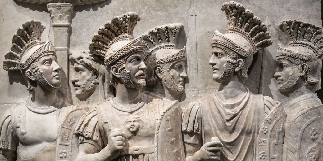 Marble relief sculpture showing Roman soldiers in detailed armor and helmets, engaged in discussion or assembly.