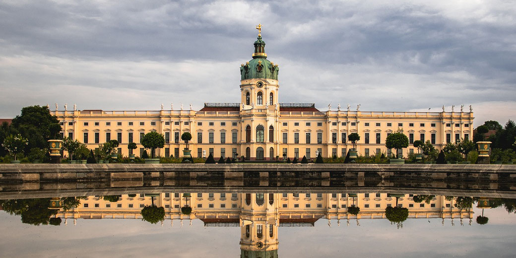 Charlottenburg Palace stands symmetrically with its reflection visible in the still water of the garden pond
