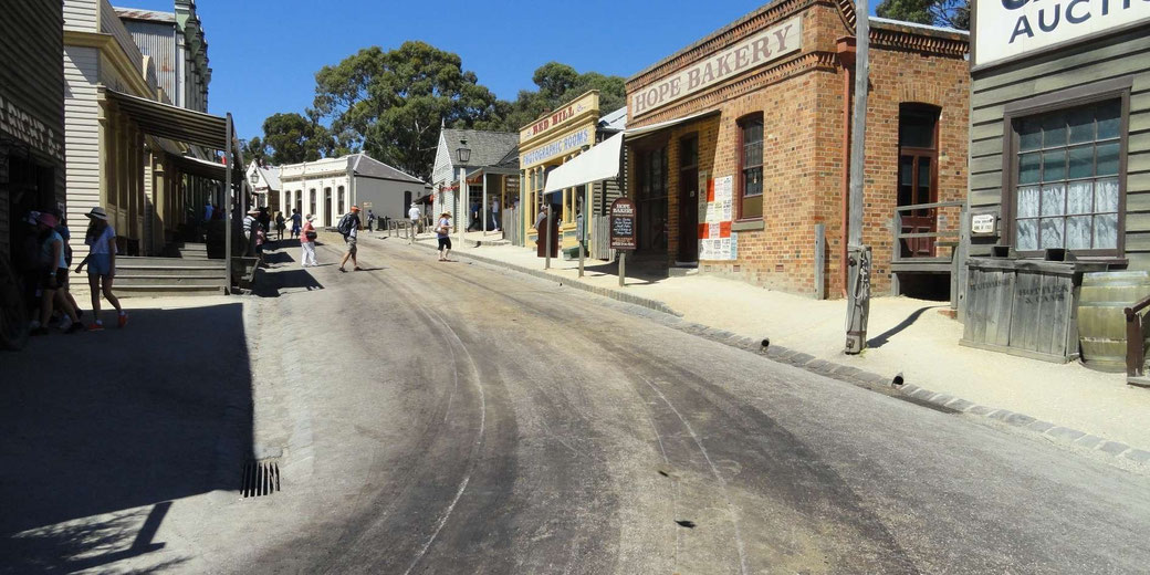 Historic street with period storefronts, brick buildings, and visitors walking under a clear sky in an old mining town.