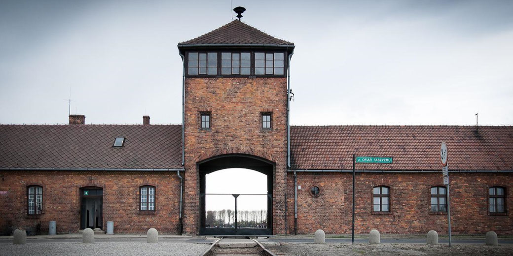 Brick entrance building of Auschwitz-Birkenau with a central watchtower and rail tracks leading through the arched gate.