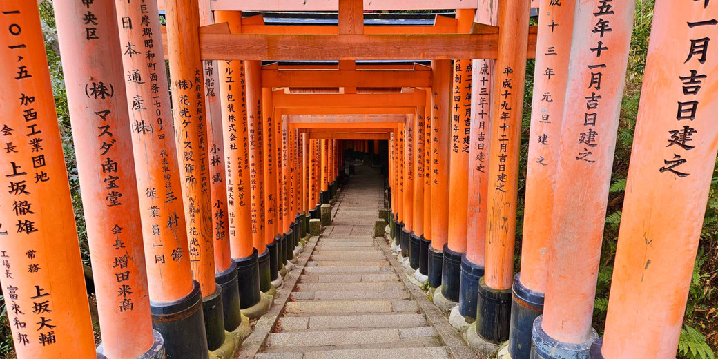 The iconic torii gate pathway at Fushimi Inari Shrine in Kyoto, Japan. The vibrant orange gates, inscribed with Japanese characters, create a mesmerizing tunnel along a stone stairway.