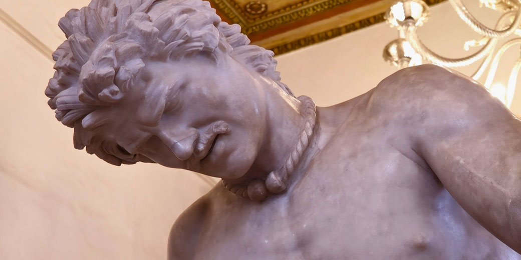 Marble statue of a wounded man with a rope necklace, head bowed in pain or defeat, capturing a moment of sorrow.