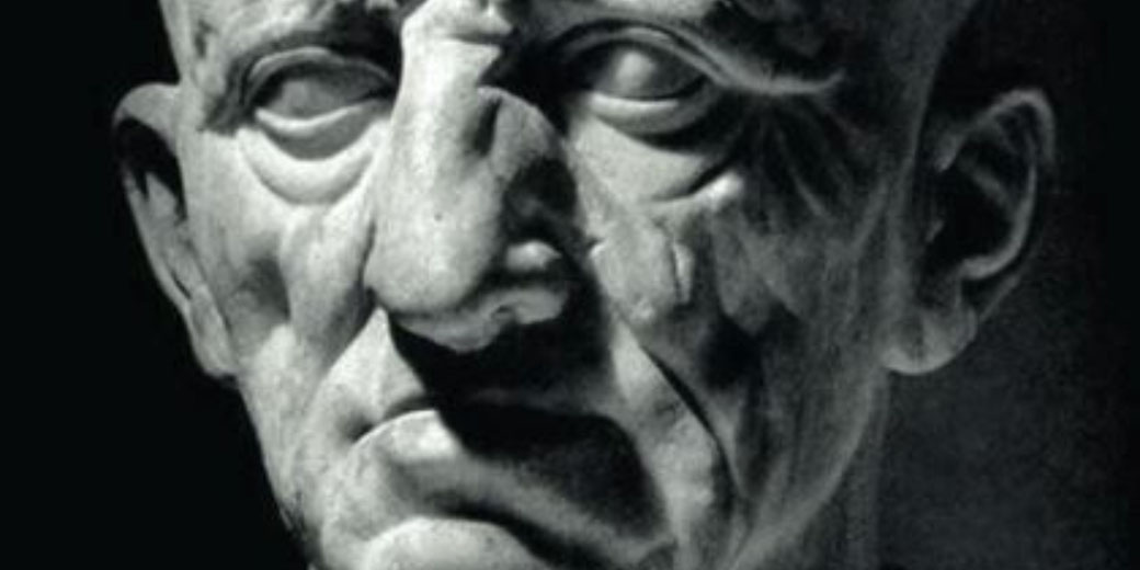 Close-up of an ancient Roman marble bust showing an older man's deeply lined face with a stern expression.