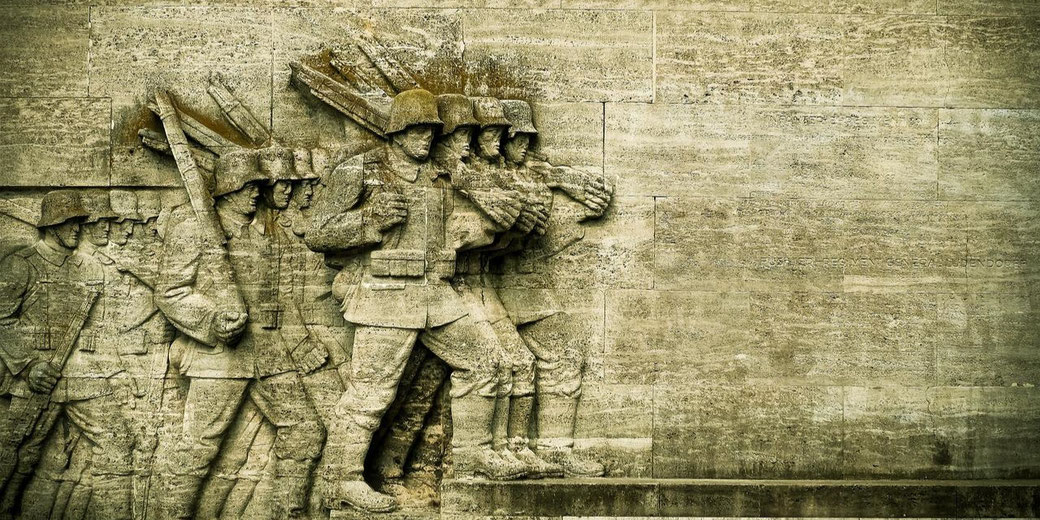 Stone relief sculpture of marching soldiers in uniform with rifles, carved into a large textured wall.
