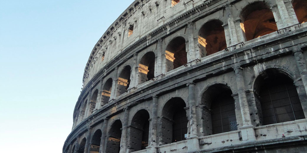 The exterior of the Colosseum in Rome, Italy. The ancient amphitheater's weathered stone arches and columns are illuminated by sunlight