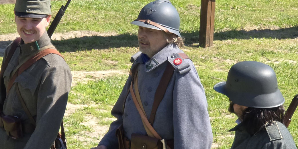 Three men in World War I military uniforms and helmets standing outdoors, appearing to participate in a historical reenactment.