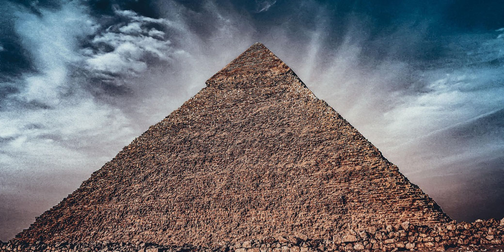 The Great Pyramid rises sharply against a dramatic sky, with textured clouds radiating outward behind its weathered stone surface.