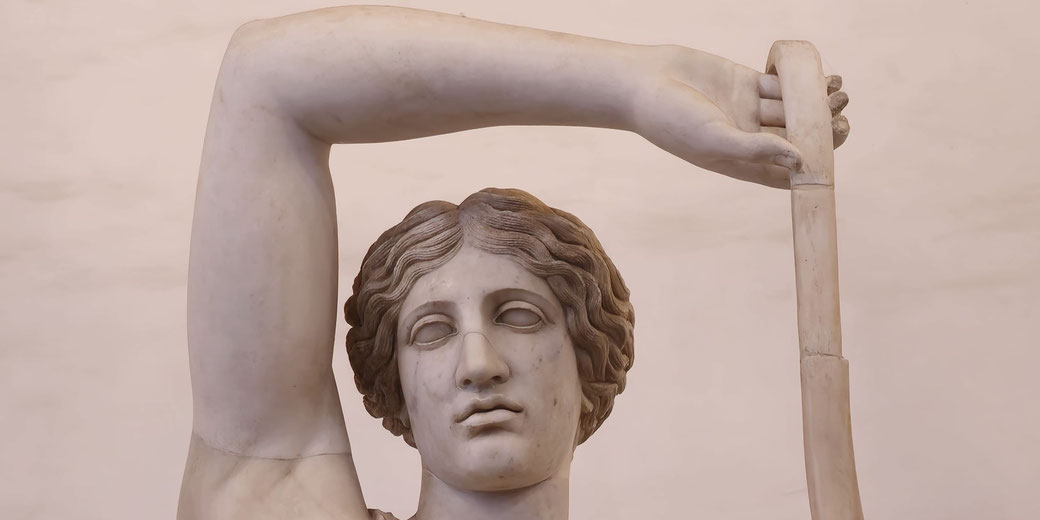 Marble statue of a woman with wavy hair, holding a curved object above her head, gazing forward with a serene expression.