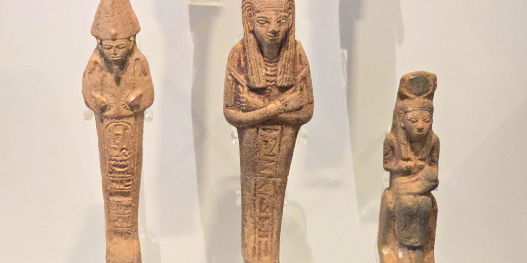Three ancient Egyptian shabti figurines, small clay statues placed in tombs to serve the deceased in the afterlife. They are inscribed with hieroglyphs and depict traditional funerary poses.