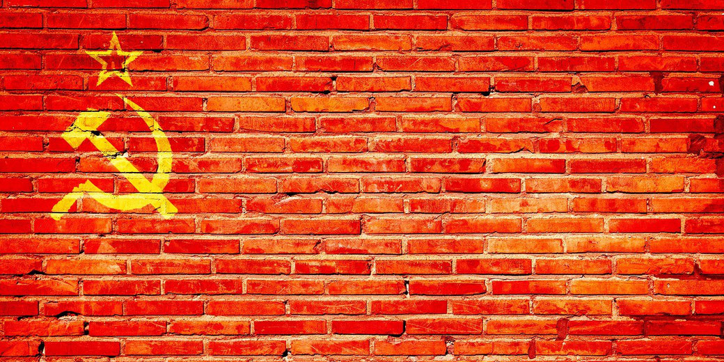 A red brick wall with a yellow hammer and sickle symbol and star painted on the left side, evoking Soviet imagery.