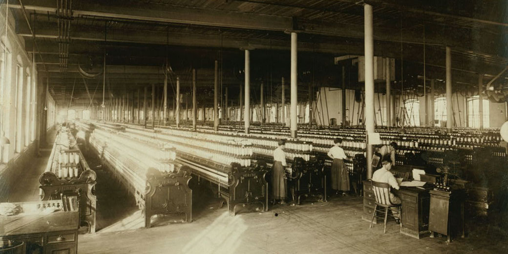 A large textile mill with rows of spinning machines, operated by workers, including women. 