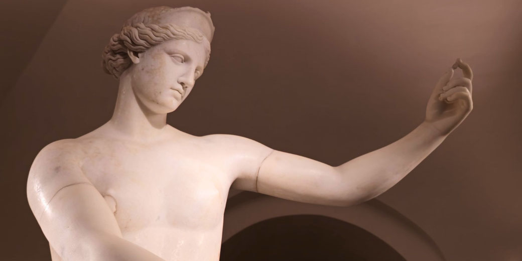 Marble statue of a graceful, youthful figure with an outstretched arm and serene expression, featuring detailed wavy hair and smooth contours.