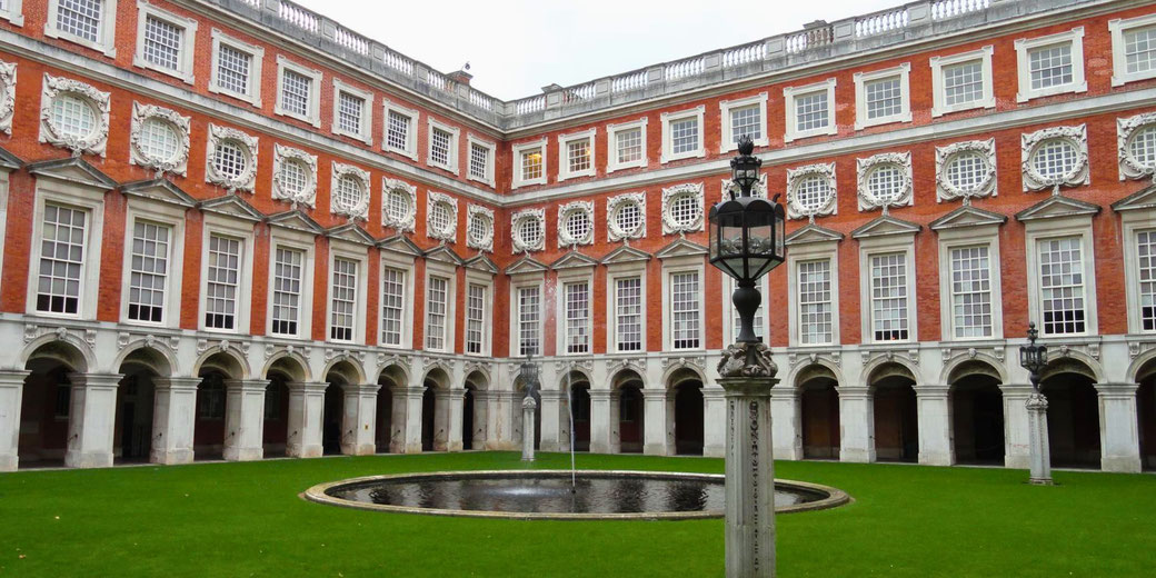 Fountain Court at Hampton Court Palace, showcasing its elegant Baroque architecture with red brick, white stone details, arched walkways, a central fountain, and classic lanterns.