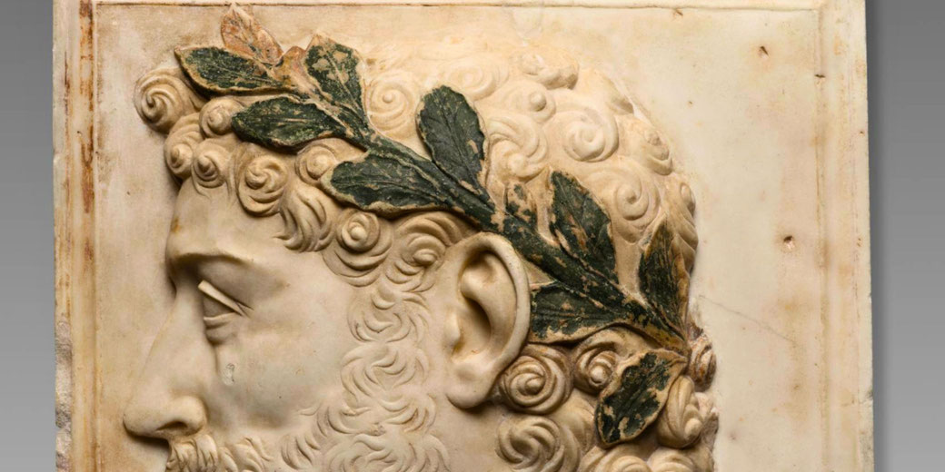 Marble bust of Emperor Antoninus Pius, featuring corkscrew curls and a laurel wreath with traces of green and gold pigment.