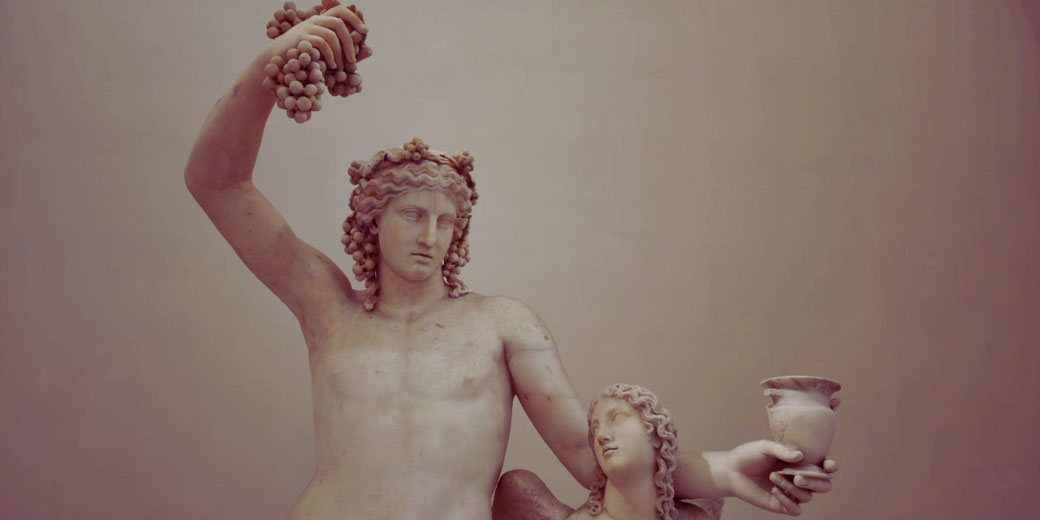 Marble statue of Dionysus holding grapes aloft, accompanied by a female figure offering a cup, symbolizing wine and revelry.