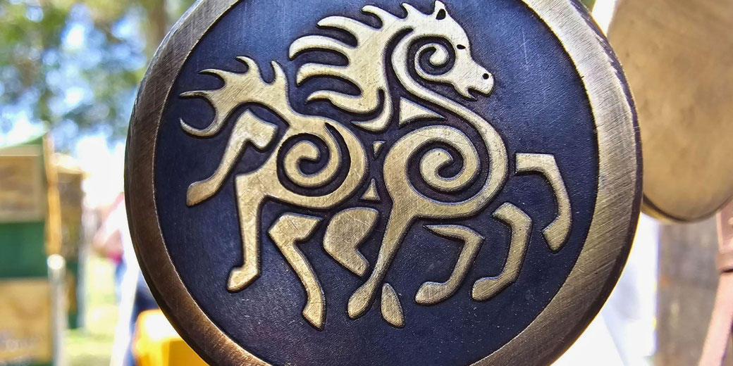 A round medallion with a stylized engraving of an eight-legged horse, inspired by Norse mythology. The gold design contrasts against a dark background, giving it an intricate, bold appearance.