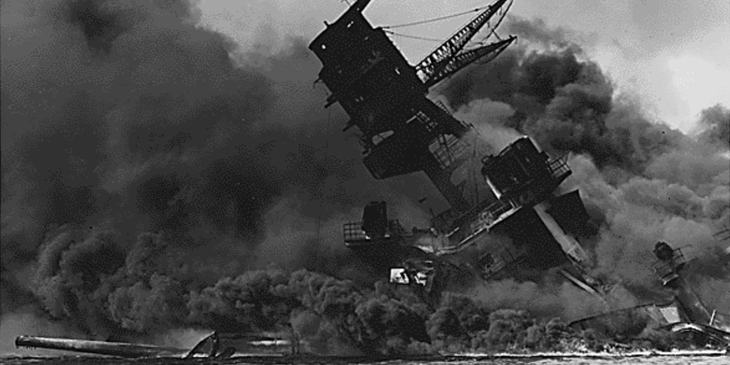 A battleship tilts heavily as thick black smoke engulfs the sky, indicating an intense and destructive explosion during wartime.
