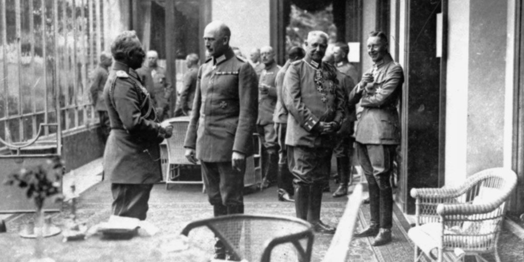 A historical black-and-white photo of German military officers in uniform, engaged in conversation on a terrace.