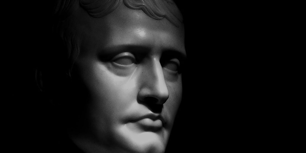 Marble bust of a man lit dramatically from the side, highlighting sharp facial features and casting deep shadows against a dark background.