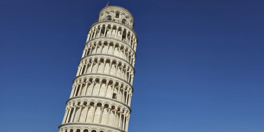 The Leaning Tower of Pisa, a white marble bell tower with Romanesque arches, tilts noticeably under a clear blue sky.