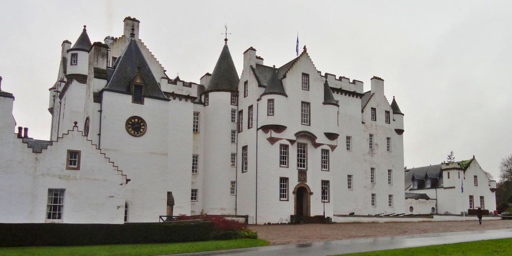 A grand, white castle with distinctive pointed towers, a clock on the front wall, and lush green grounds. 