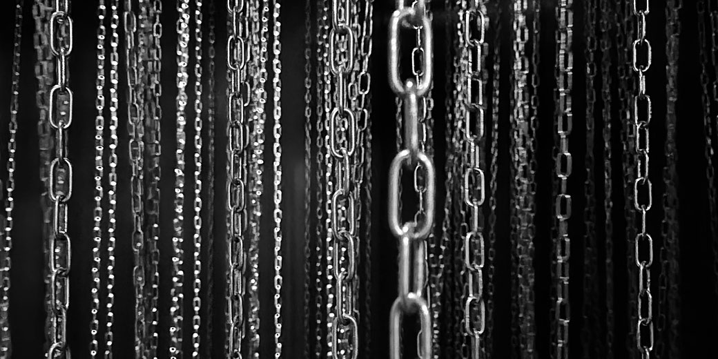 Multiple hanging chains in black and white. The varying focus and depth create a striking contrast, emphasizing texture and repetition, evoking themes of confinement or industrial design.