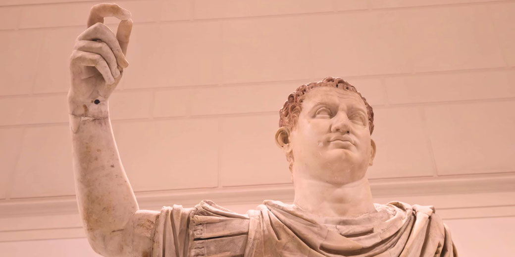 Marble statue of a Roman figure in a toga, raising one hand in a commanding gesture, with a stern and authoritative expression.