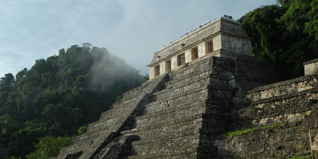 The Temple of the Inscriptions in Palenque, Mexico, a stepped Mayan pyramid surrounded by lush jungle, with mist rising over the ruins, creating a mysterious atmosphere.