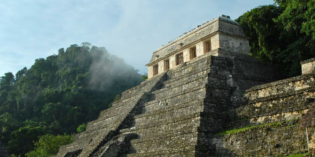 The Temple of the Inscriptions in Palenque, Mexico, a stepped Mayan pyramid surrounded by lush jungle, with mist rising over the ruins, creating a mysterious atmosphere.