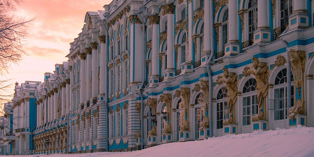 A grand palace facade features blue and white columns, gold accents, and statues, set against a snowy foreground and pink sky.