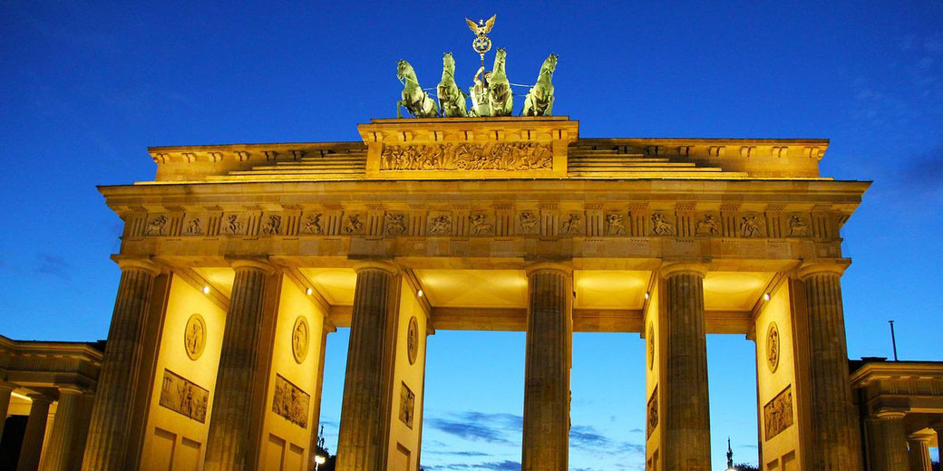 The illuminated Brandenburg Gate with its columns and chariot sculpture stands against a deep blue evening sky.