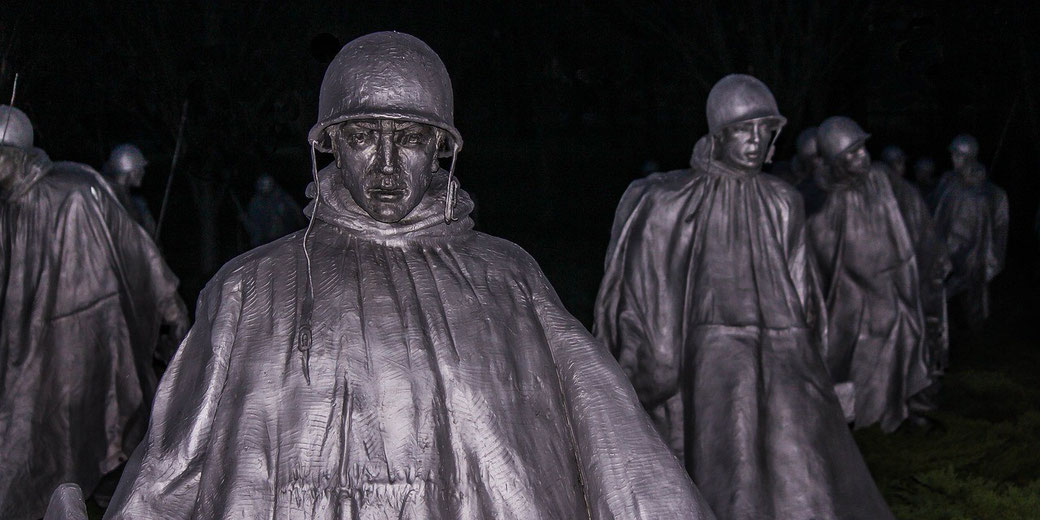 Lifelike soldier statues in rain gear march through darkness, evoking a somber and powerful presence.