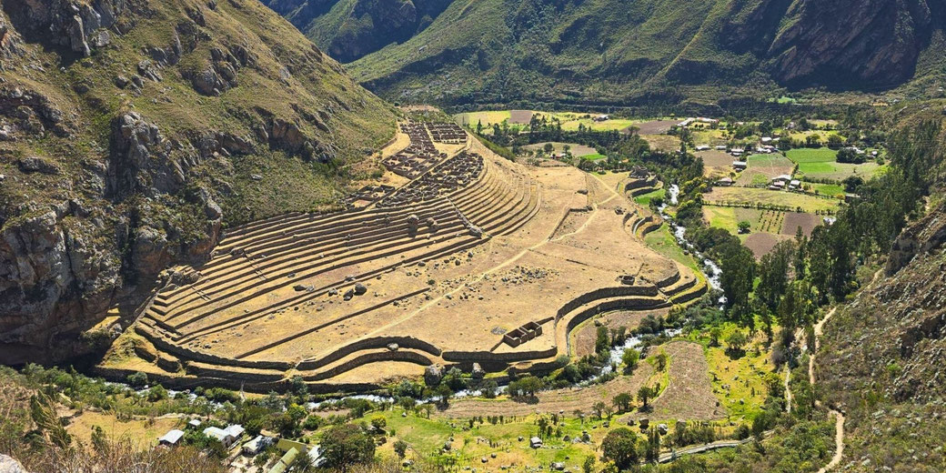 The Incan ruins of Llactapata in Peru, featuring terraced agricultural fields and ancient stone structures set in a lush valley surrounded by steep mountains.