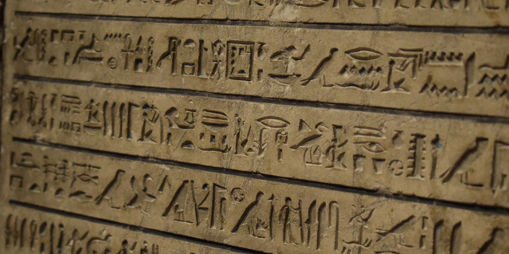 Ancient Egyptian hieroglyphs carved into a stone surface, arranged in horizontal lines. The inscriptions feature birds, symbols, and characters, likely part of a historical or religious text.