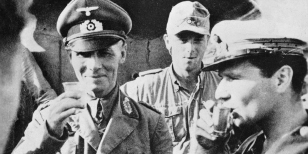 German officers drink from small cups while taking a break during World War II, captured in a candid black-and-white moment.