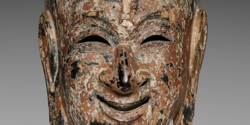 Painted wooden gigaku mask of a young Persian boy with a smiling face and chipped black, reddish-brown, and gray surface.