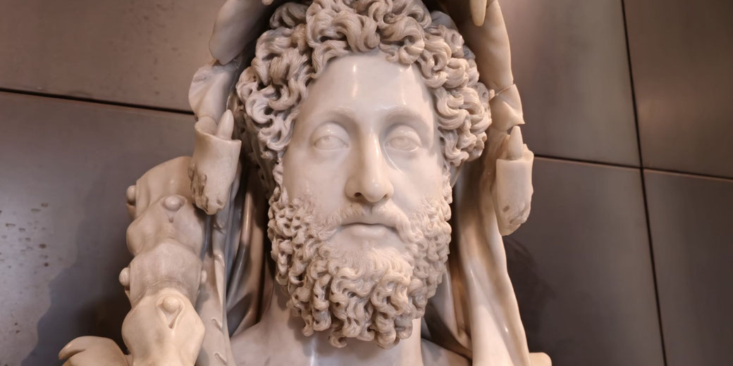 Close-up of a marble statue of a bearded man with curly hair, wearing a lion skin headdress, holding a club over his shoulder.