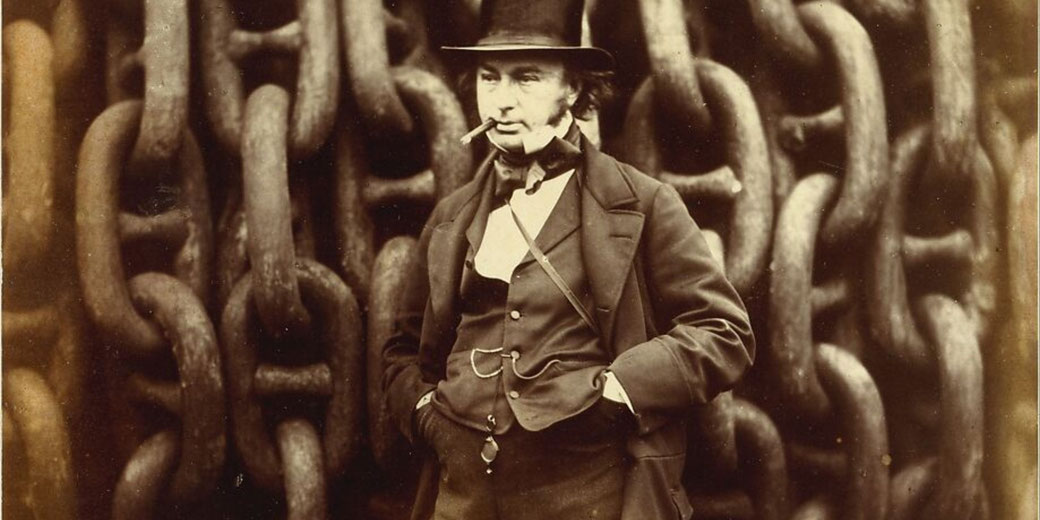 A man in a suit, top hat, and pocket watch stands confidently in front of massive iron chains, smoking a cigar.