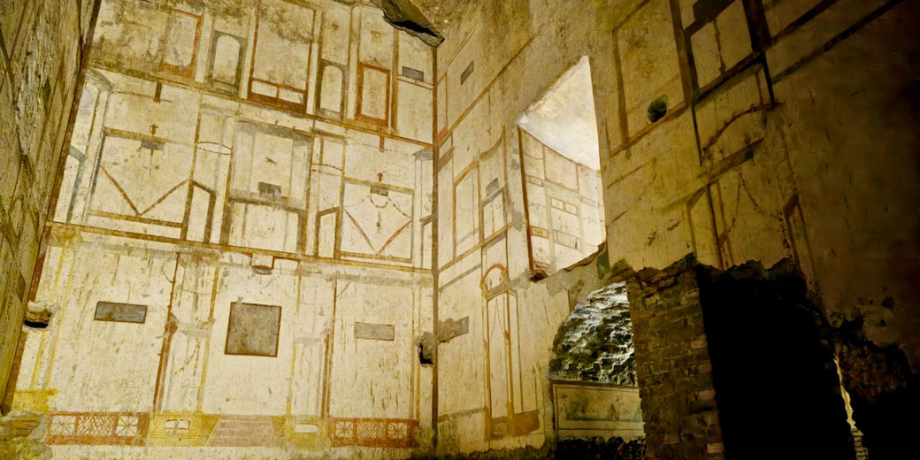 Ancient Roman room with faded wall frescoes in geometric patterns, lit by soft light, showing signs of age and partial damage.