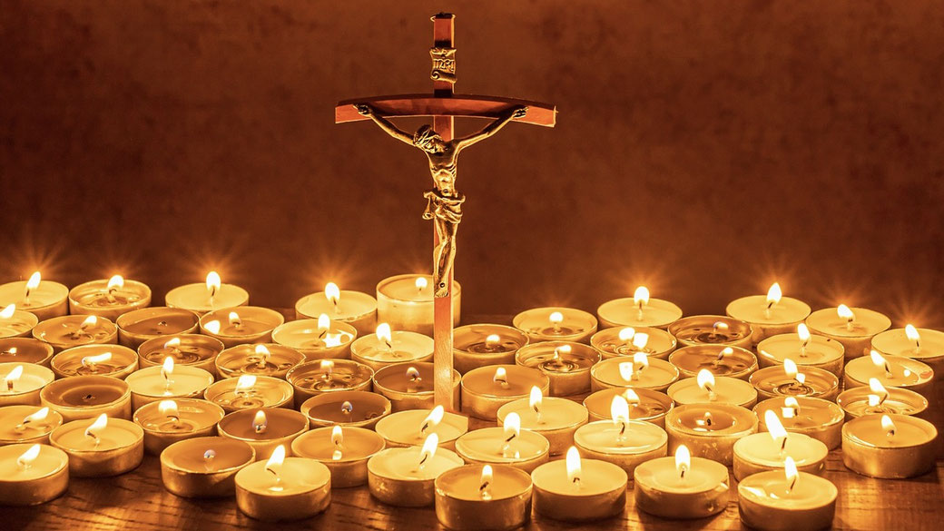 Wooden crucifix surrounded by glowing tea light candles, creating a warm and reverent atmosphere.