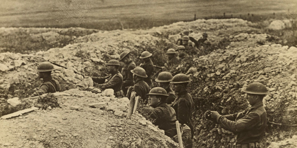 World War I soldiers in helmets manning a trench line, surrounded by rough earth and debris.