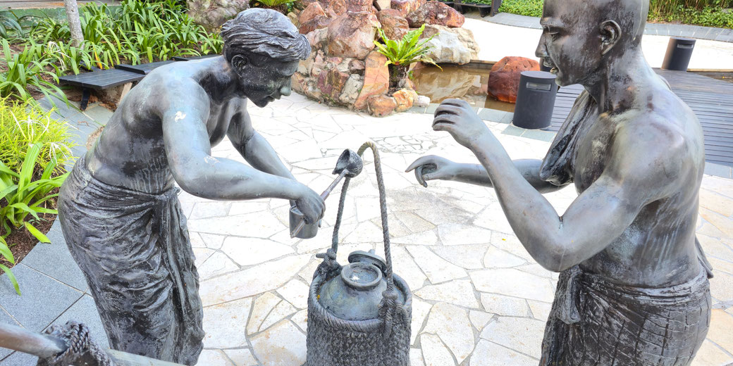 Two bronze statues depict a traditional scene of water collection using a ladle and pot.