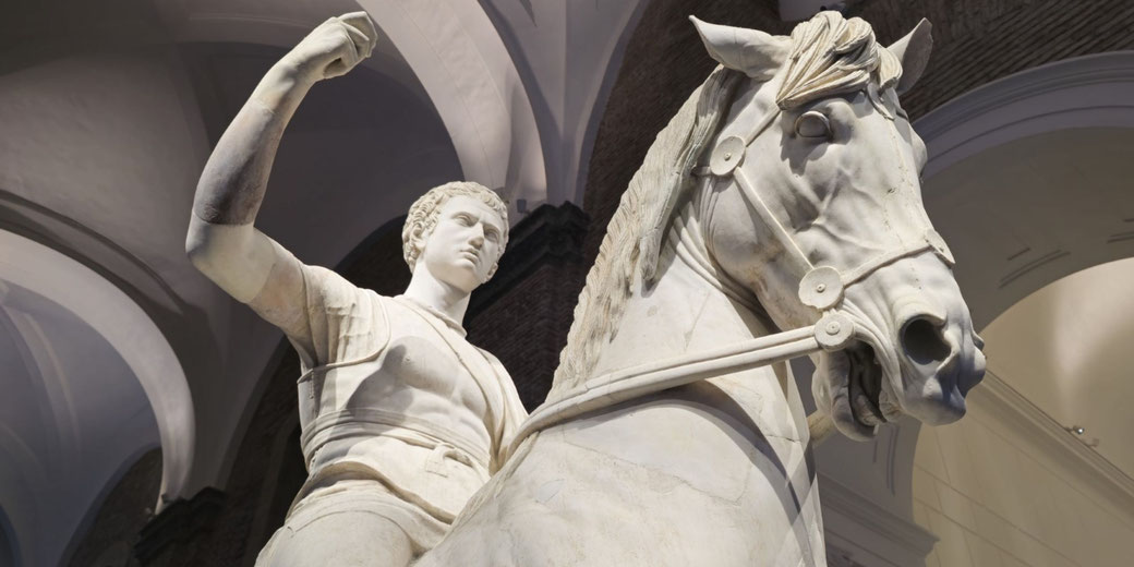 Marble statue of a young man on horseback, arm raised, with detailed facial features and a dynamic pose, viewed from a dramatic low angle.