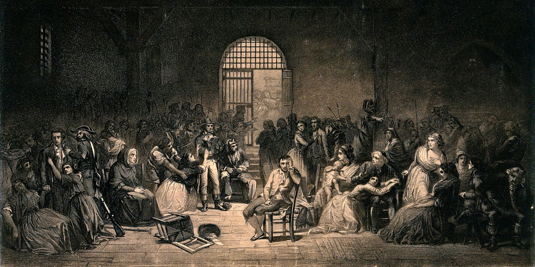 A crowded prison scene, likely from the French Revolution. A distressed prisoner sits in the center, surrounded by others in despair, while guards and onlookers fill the dark, oppressive space.