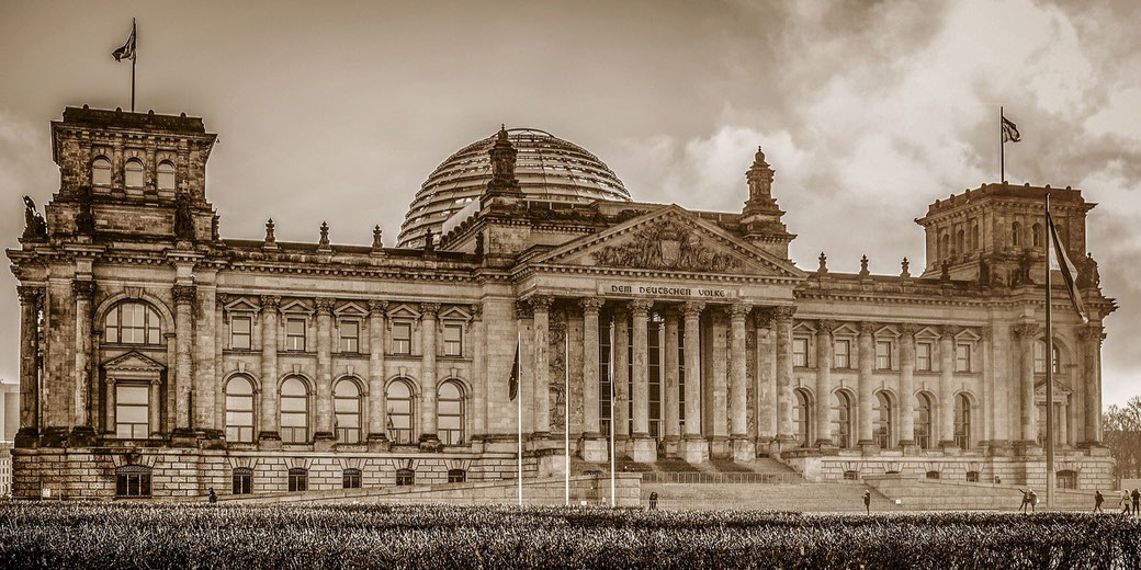 The Reichstag building stands with its grand facade and glass dome under a cloudy sky in sepia tones.