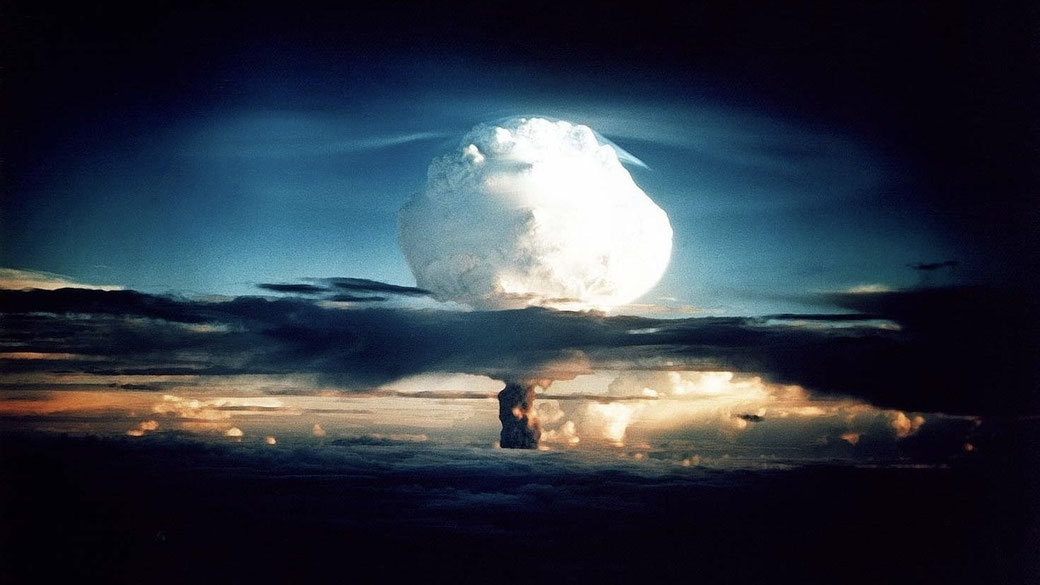 Massive mushroom cloud rises into the sky during a nuclear explosion, with layered clouds and fiery illumination below.