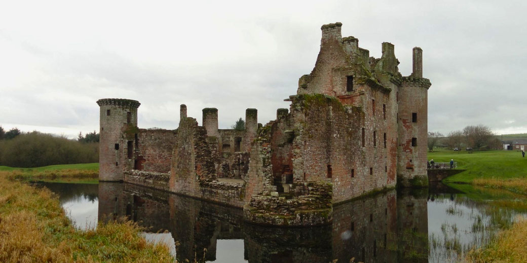 The ruins of Caerlaverock Castle, a partially collapsed medieval fortress surrounded by a moat, with weathered stone walls and turrets, evoking a sense of history and resilience.