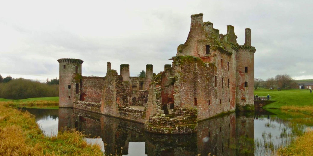 The ruins of Caerlaverock Castle, a partially collapsed medieval fortress surrounded by a moat, with weathered stone walls and turrets, evoking a sense of history and resilience.